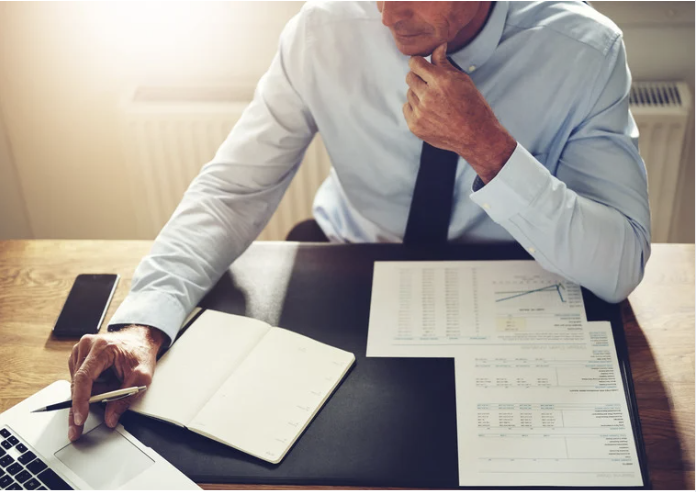 A man sitting at a desk with a laptop and financial documents